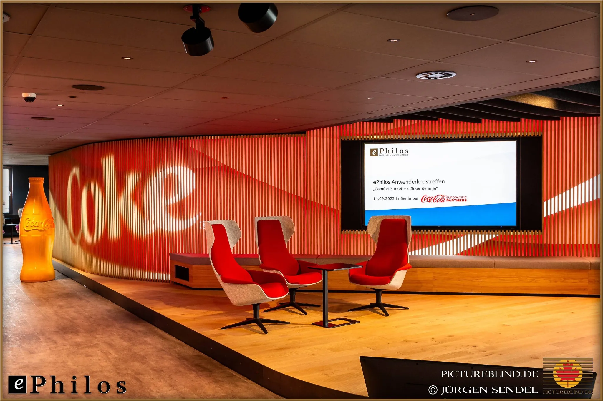 Modern conference room with red chairs and a large screen, decorated with Coca-Cola themes, prepared for the Ephilos user group meeting in Berlin