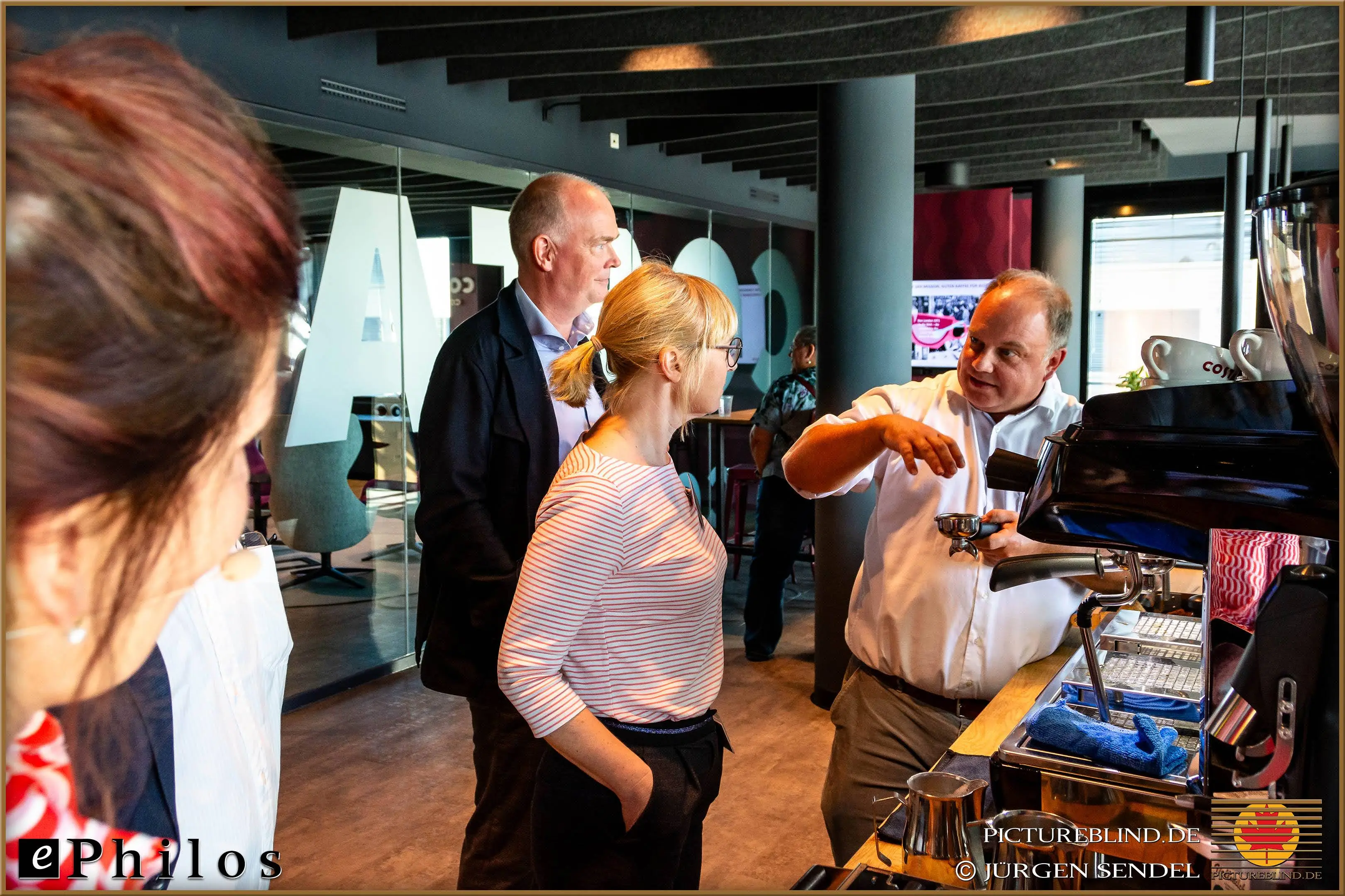 Group of participants receiving a demonstration at a coffee machine during a networking break in a modern conference area