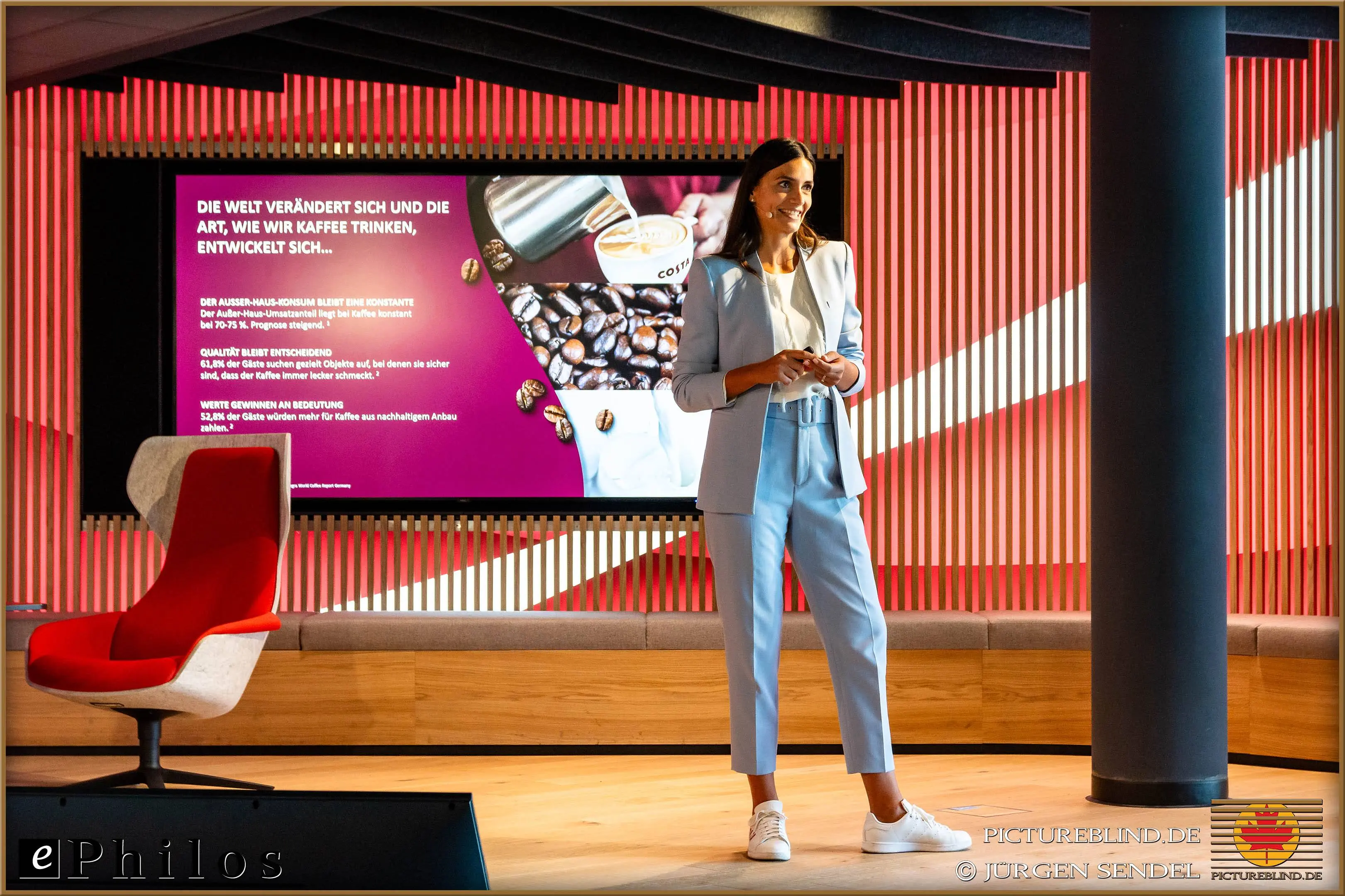 Presenter in a light blue suit giving a talk about the evolution of coffee consumption in front of a screen at a conference